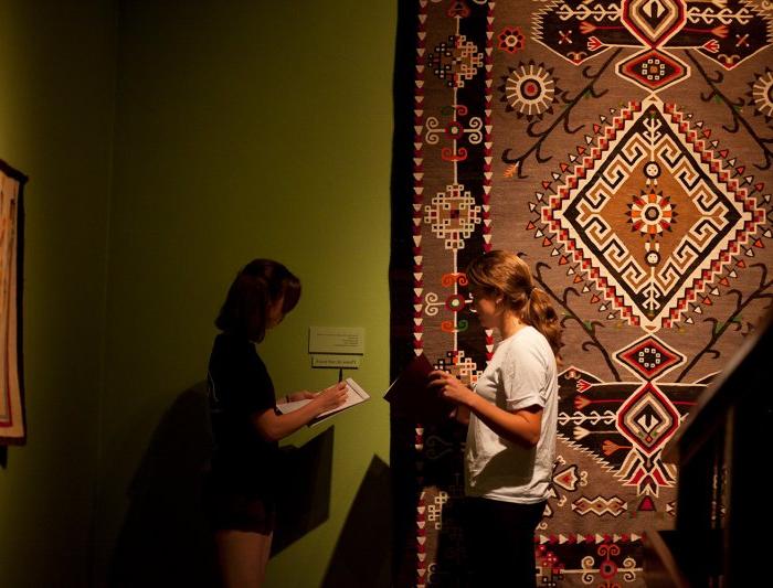 photo of two students taking notes in front of a piece of textile art in the museum